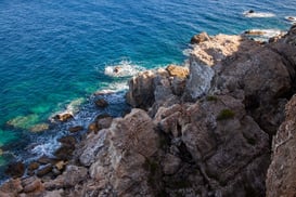 brown rocky mountain beside blue sea during daytime