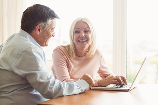 Happy mature couple using laptop at home in the kitchen